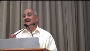 An older Latino speaks at a podium