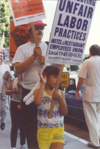 a young girl walks at the front of a march carrying a sign reading "Unfair Labor Practices - Hotel & Restaurant Employees Union Local 11, AFL-CIO - Beverly Rodeo Unfair"