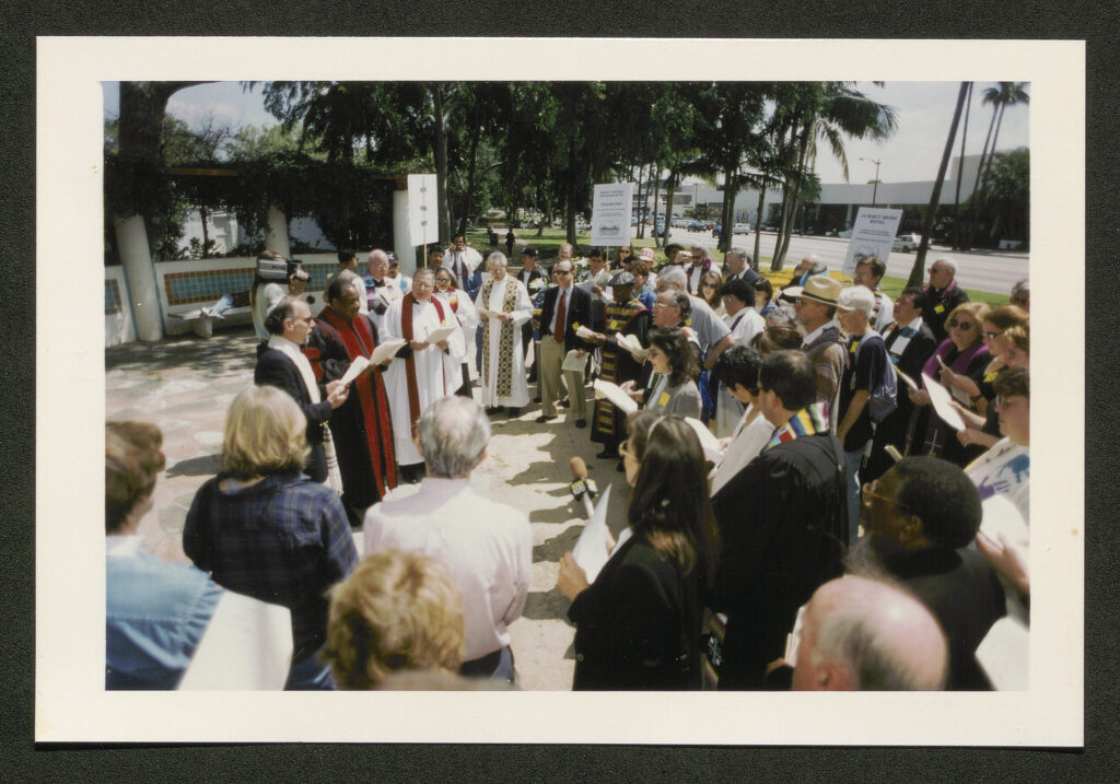 A group of clergy, wearing robes and vestments, gathered in a circle in prayer. 