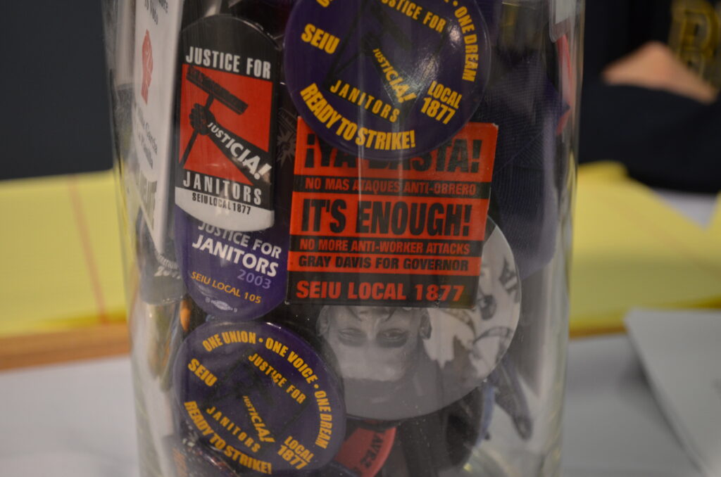 close up photograph of a plastic container full of union buttons from various campaigns and actions of the Justice for Janitors