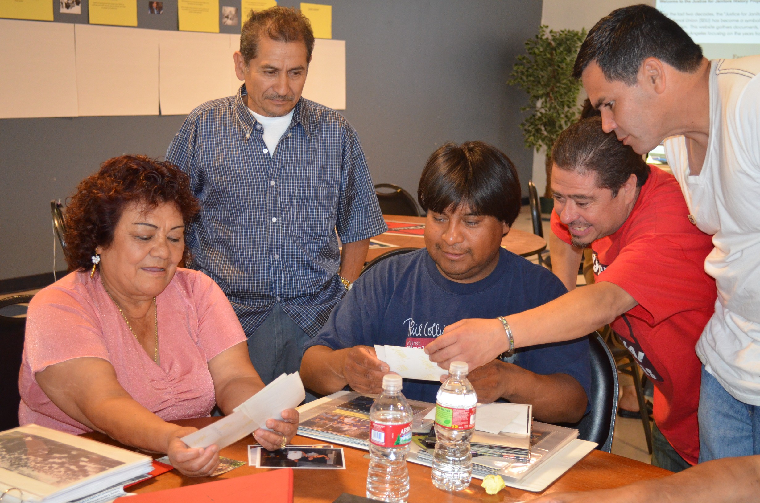 A small group of janitors sits around a table sharing photos documenting the history of their union.