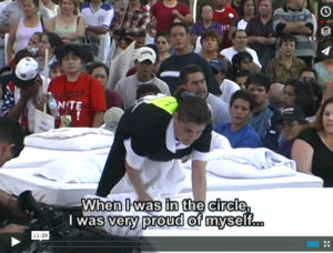Screenshot from a documentary film shows a hotel maid making the bed in the street while a crowd looks on. The screenshot includes a caption reading "When I was in the circle, I was very proud of myself..."