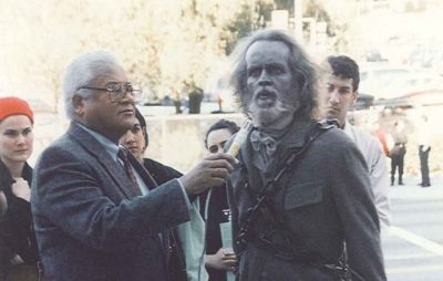 On the right, Dave Clennon dressed in a full costume, complete with chains and make up, addressing the media as Jacob Marley on his way to address the City Council. Rev. James Lawson holds the microphone for him.